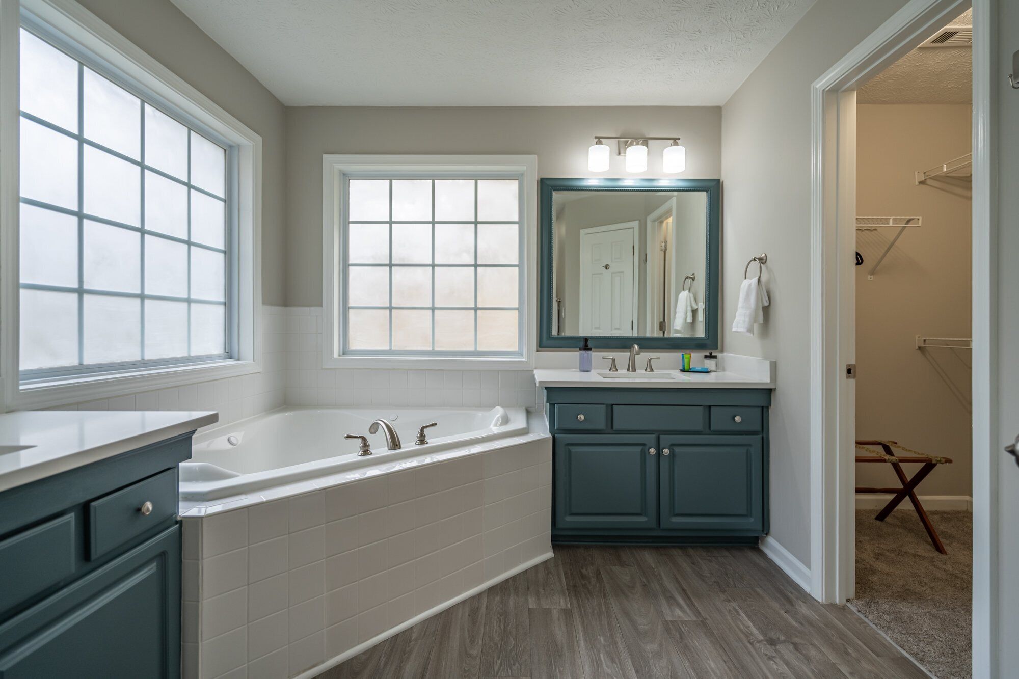 A bathroom with a bathtub, a sink, and a mirror. There is a window and a door leading to another room.