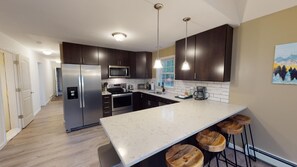A modern kitchen with dark cabinets, stainless steel appliances, a marble countertop, and wooden stools. - The Mendon House (Killington)