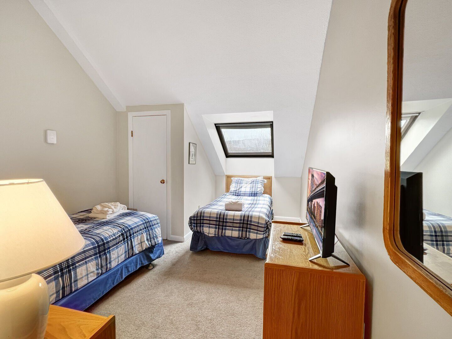 Een ruime, goed verlichte kamer met twee bedden, een bureau, een spiegel en een dakraam.