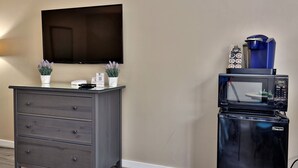 Ein Zimmer mit dunklem Holzschrank, einem flachbildfernseher an der Wand und einem schwarzen Kühlschrank mit Kaffeemaschine obenauf.