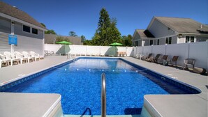 Ein rechteckiger Pool mit einer Metallleiter in der Mitte, umgeben von weißen Liegestühlen und grünen Sonnenschirmen.