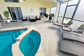 Ein Innenpoolbereich mit Liegestühlen, einem Grill und Blick ins Freie.