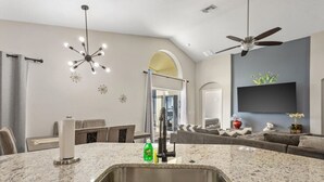 A modern kitchen with a granite countertop, stainless steel sink, and a ceiling fan. - NEW King Bed Glow In The Dark Kid Cave (Kissimmee)