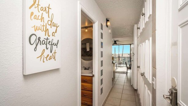 A hallway with a motivational quote on the wall, a door leading to a bathroom, and a view of the outside. - Beach Retreat Walk to Surf & Dining (Kihei)