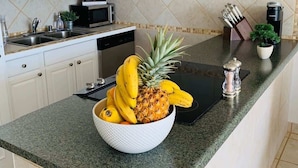 A kitchen with white cabinets, a granite countertop, a microwave, a coffee maker, and a bowl of fruit. - Beach Retreat Walk to Surf & Dining (Kihei)