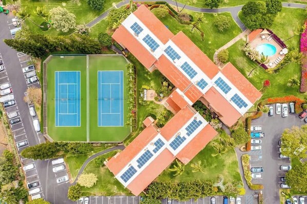An aerial view of a property with a tennis court, a swimming pool, and a parking lot.