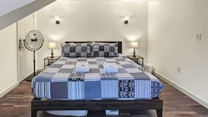 Un dormitorio con una cama, dos lámparas de noche, un ventilador de pie y un ventilador de techo.