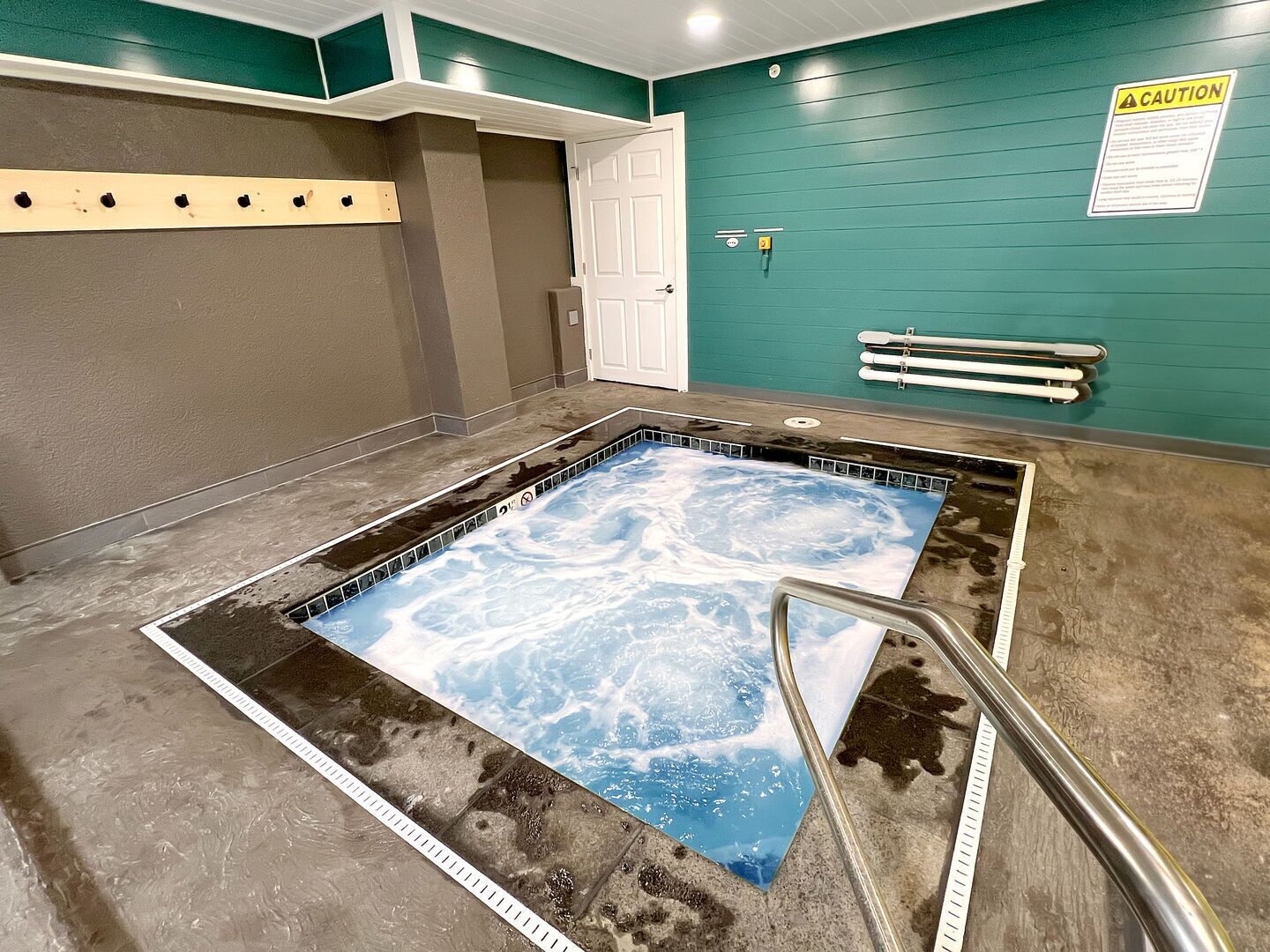 A hot tub with a blue foam cover, a metal ladder, and a caution sign on the wall.