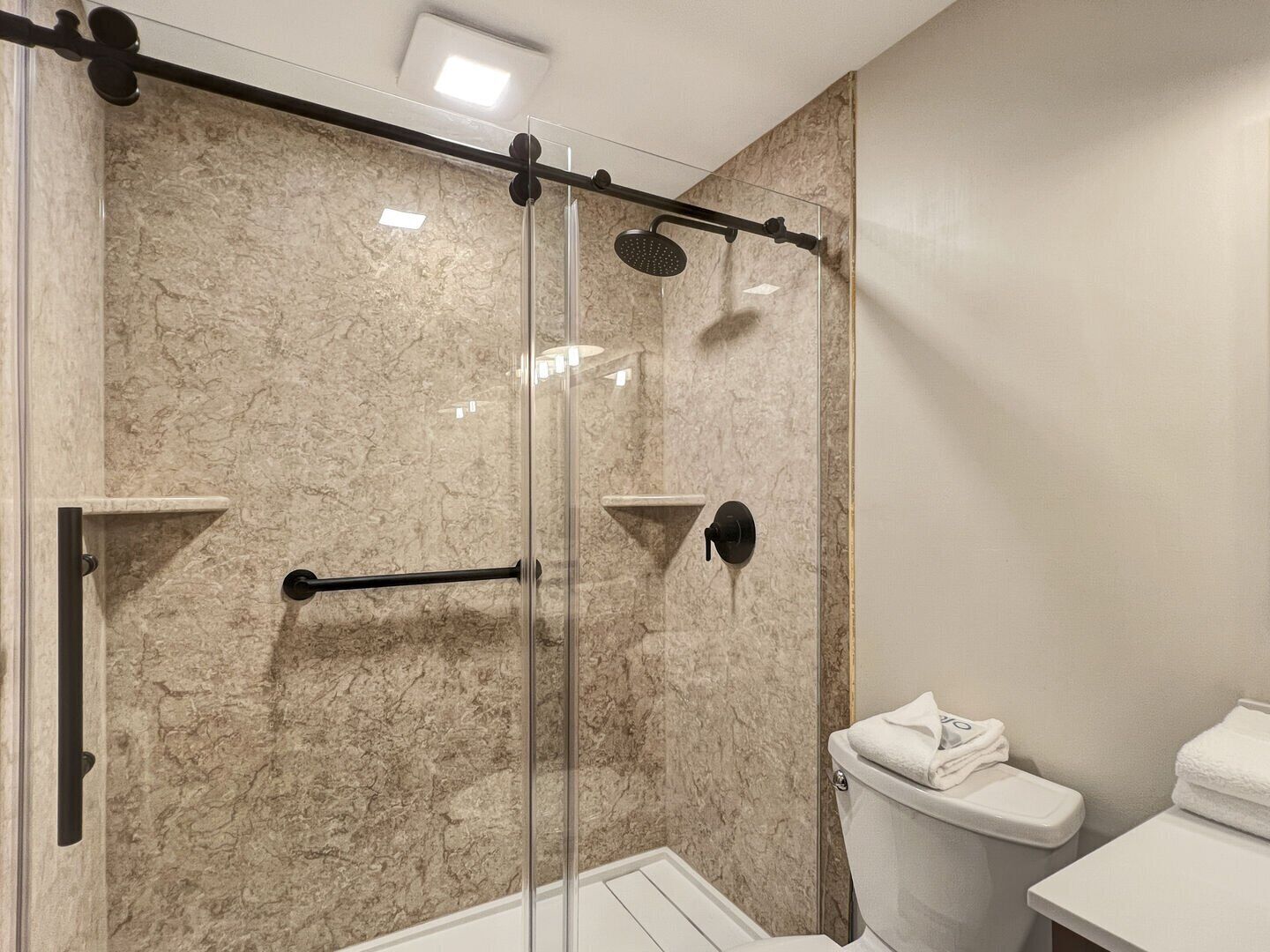 A modern bathroom with a glass-enclosed shower, marble walls, and a white toilet.