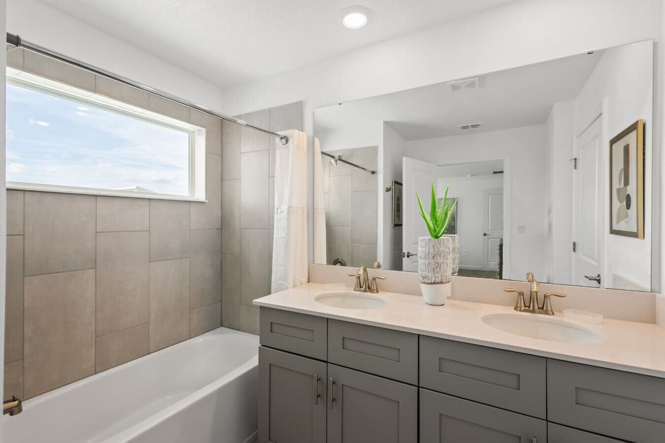 A modern bathroom with two sinks, a large mirror, and a bathtub.
