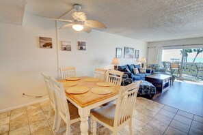 A dining area with a wooden table and white chairs, a ceiling fan, and a view of the ocean through large windows. - 428 El Matador (Fort Walton Beach)