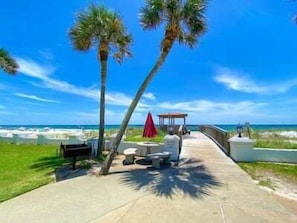 A paved pathway leading to a beach area with a gazebo, palm trees, and outdoor seating. - 454 El Matador (Fort Walton Beach)