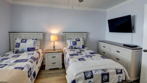 Un dormitorio con dos camas, ventilador de techo, televisor y lámpara de noche.