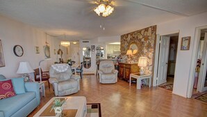 A spacious living room with a blue sofa, two armchairs, a coffee table with a plant, a chandelier, and a stone accent wall. - 555 El Matador (Fort Walton Beach)