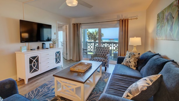 A modern living room with a flat-screen TV, a white cabinet, a patterned armchair, a dark sofa, and a view of the ocean through large windows. - 427 El Matador (Fort Walton Beach)