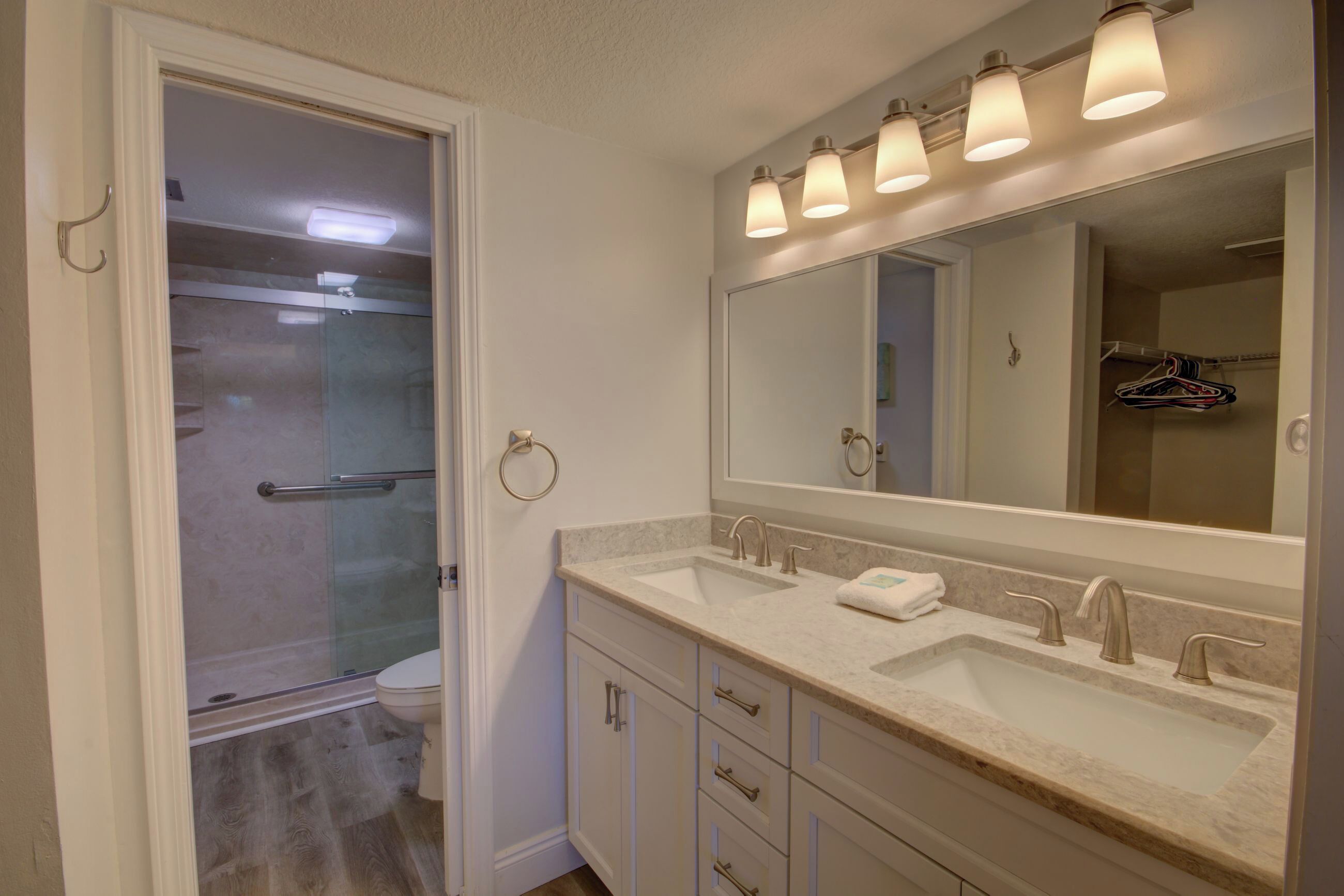 A bathroom with a glass shower enclosure, a double sink vanity, and a large mirror.