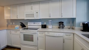 A kitchen with white cabinets, a microwave, a stove, a toaster, a blender, and a coffee maker. - 427 El Matador (Fort Walton Beach)