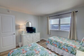 Une chambre avec deux lits, une commode, un téléviseur et une fenêtre avec des rideaux.