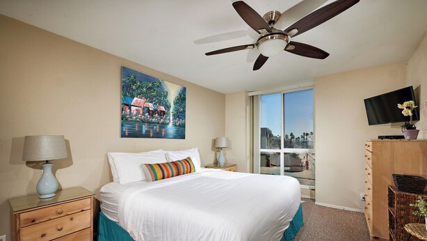 A hotel room with a bed, a ceiling fan, a painting, a TV, and a window with a view. - North Coast Village D204 (Oceanside)