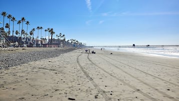A beach with a long pier extending into the ocean, palm trees lining the shore, and footprints in the sand.