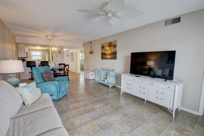 A spacious living room with a large TV, a ceiling fan, and a dining area in the background. - 527 El Matador (Fort Walton Beach)