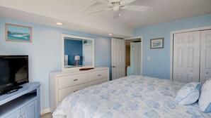 Un dormitorio con cama, cómoda, televisor y ventilador de techo.