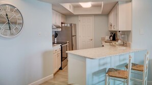 Una cocina moderna con armarios blancos, una isla grande con taburetes y un reloj de pared.