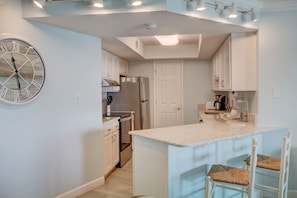A modern kitchen with white cabinets, a built-in oven, and a large island with bar stools. - 435 El Matador (Fort Walton Beach)