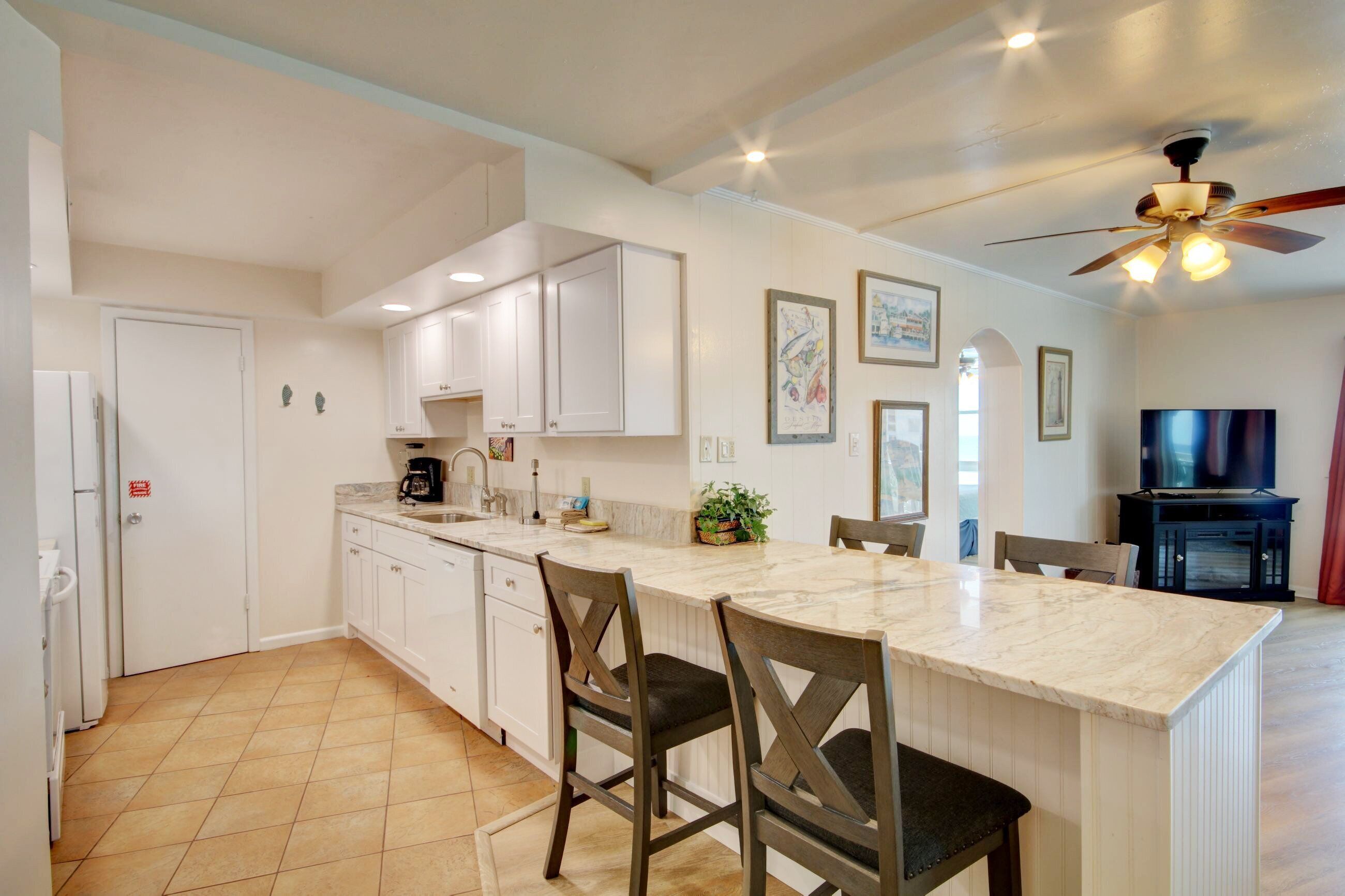 A kitchen with white cabinets, a marble countertop, and a ceiling fan.
