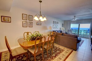 A dining area with a wooden table and chairs, a chandelier, and a view of the ocean through a balcony. - 362 El Matador (Fort Walton Beach)