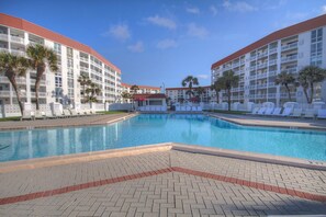Un espace piscine d’hôtel avec des bâtiments à deux étages, des palmiers et des chaises longues.
