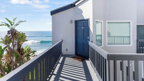 Ein Küstengebäude mit einer blauen Tür, einem Balkon mit Holzgeländer und Blick auf das Meer.