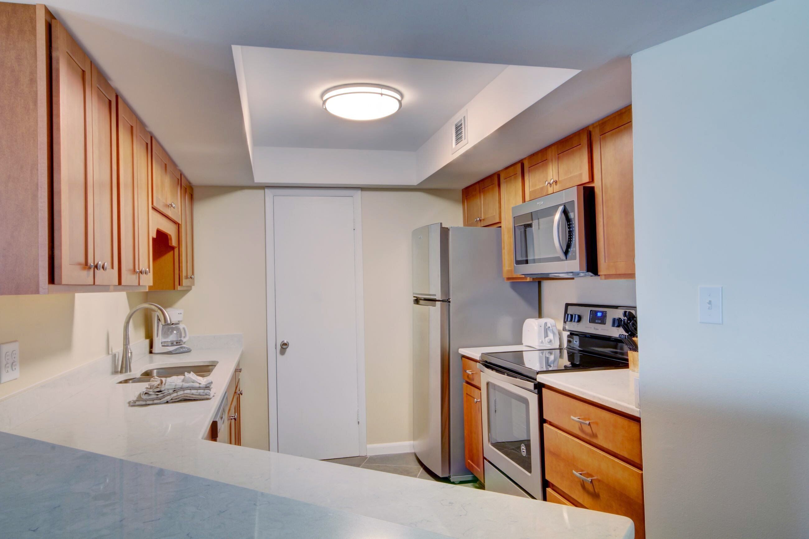 A compact kitchen with wooden cabinets, a microwave, a refrigerator, and a stove.