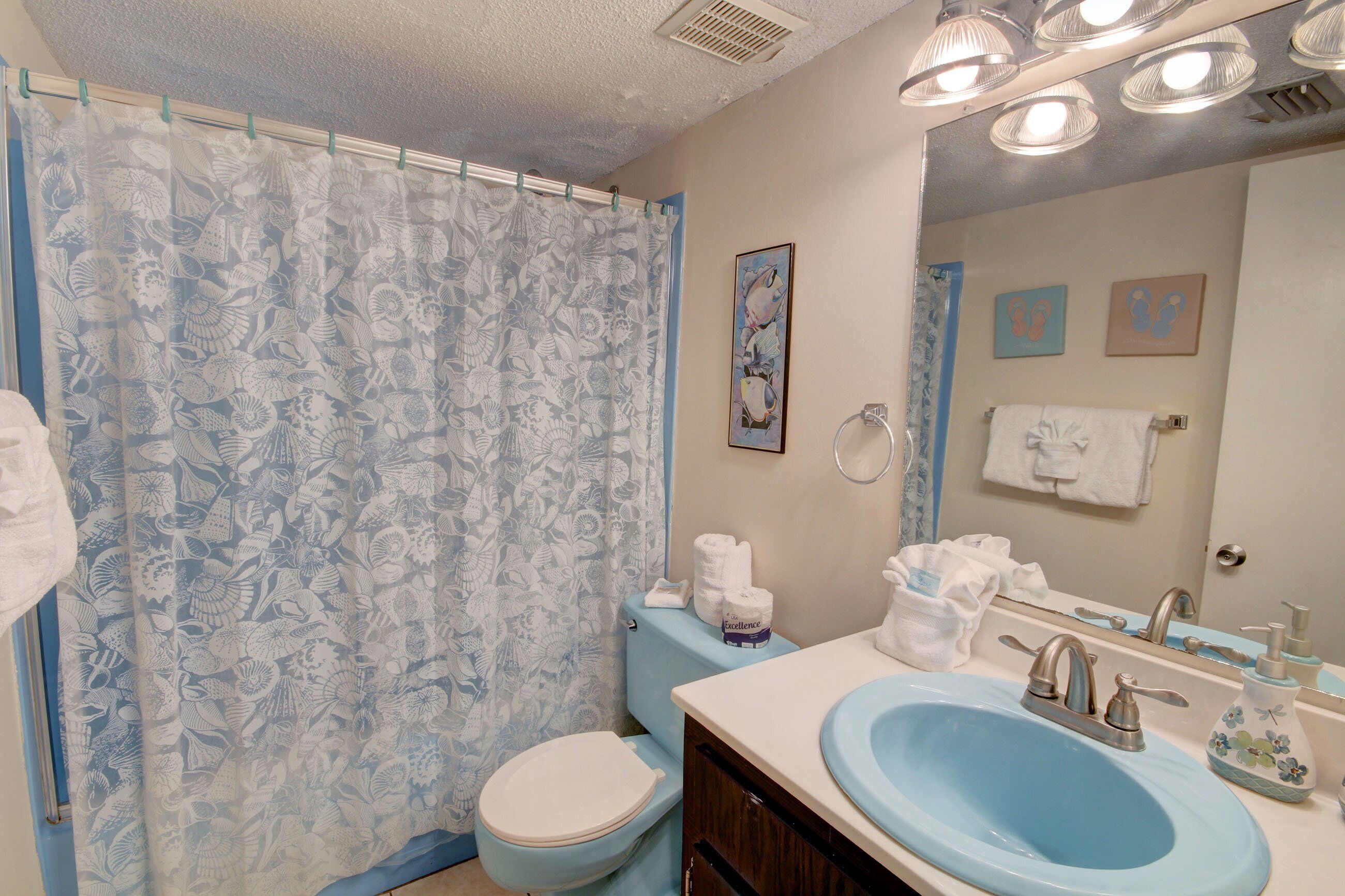 A bathroom with a blue sink, toilet, and shower curtain with a floral pattern. There are towels and toiletries on the counter.