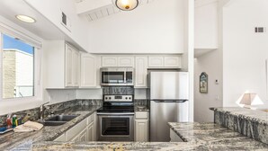 Cozinha moderna com armários brancos, bancadas de granito, eletrodomésticos de aço inoxidável e uma janela que oferece iluminação natural.