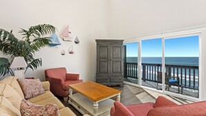 Uma sala de estar com vista para o oceano, um armário cinzento e um sofá bege.