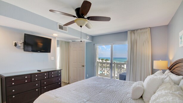 A hotel room with a bed, a ceiling fan, a TV mounted on the wall, a dresser, a balcony with a view of the ocean, and a window with curtains. - 448 El Matador (Fort Walton Beach)