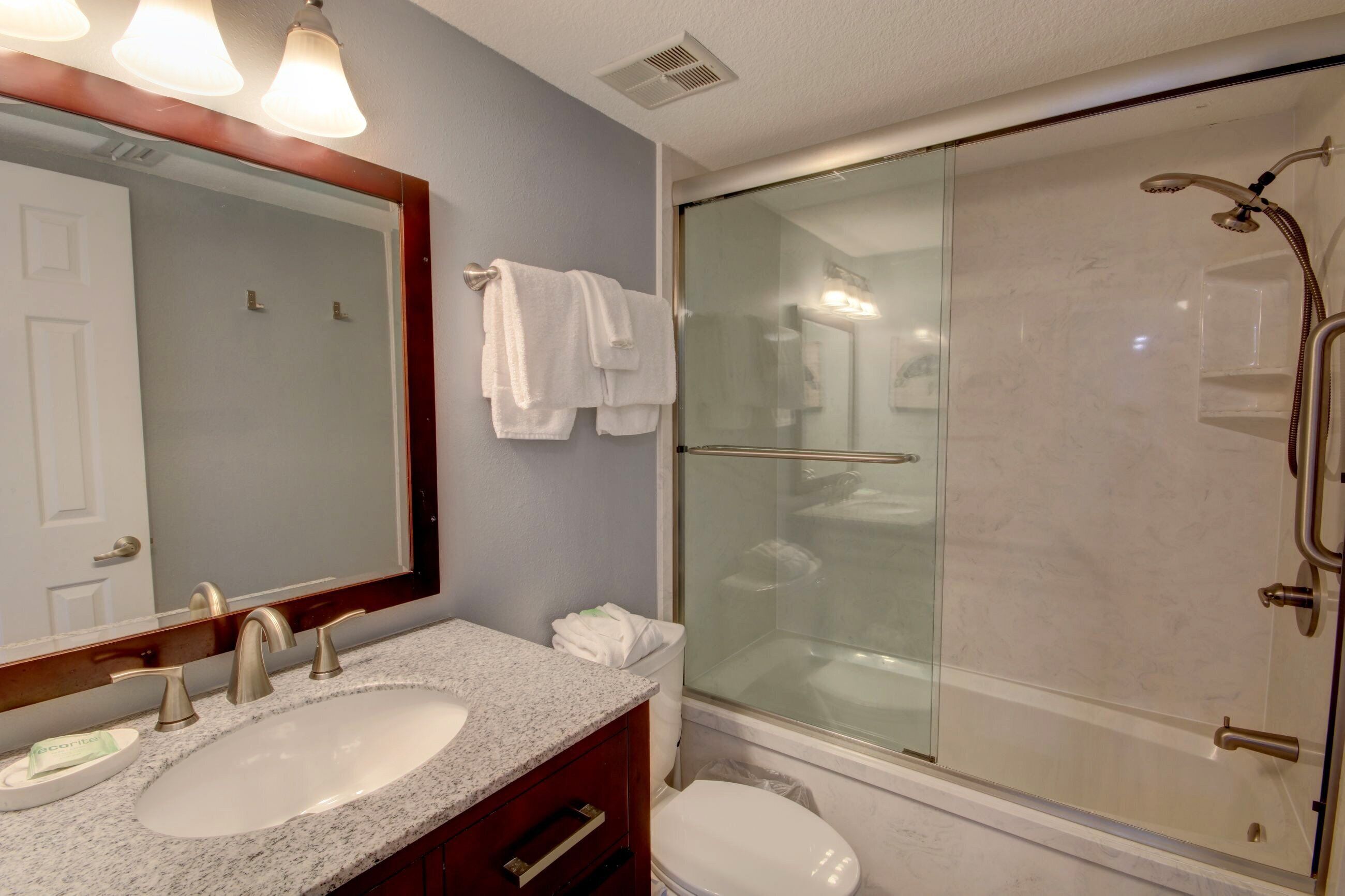 A bathroom with a double sink, a large mirror, a glass-enclosed shower, and a toilet.