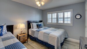 A bedroom with two beds, a ceiling fan, a nightstand with a lamp, a window with blinds, and a mirror on the wall. - 448 El Matador (Fort Walton Beach)