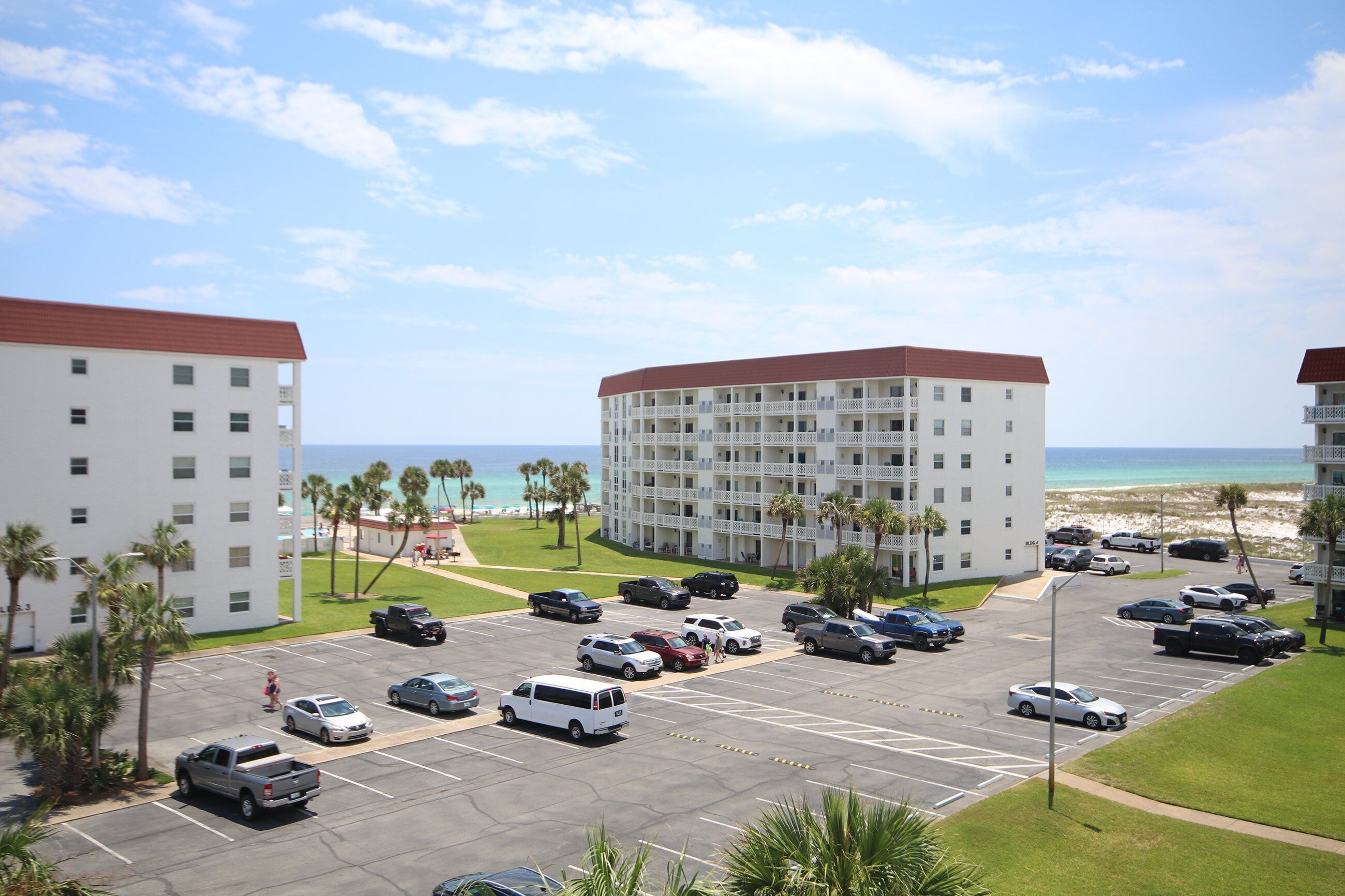 A hotel with a parking lot, multiple floors, and a view of the beach.