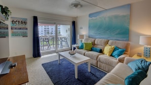 A living room with a sofa, coffee table, and a painting of a wave. - 141 El Matador (Fort Walton Beach)
