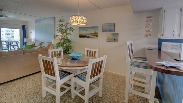 A dining area with a round table, white chairs, and a hanging light fixture. - 141 El Matador (Fort Walton Beach)