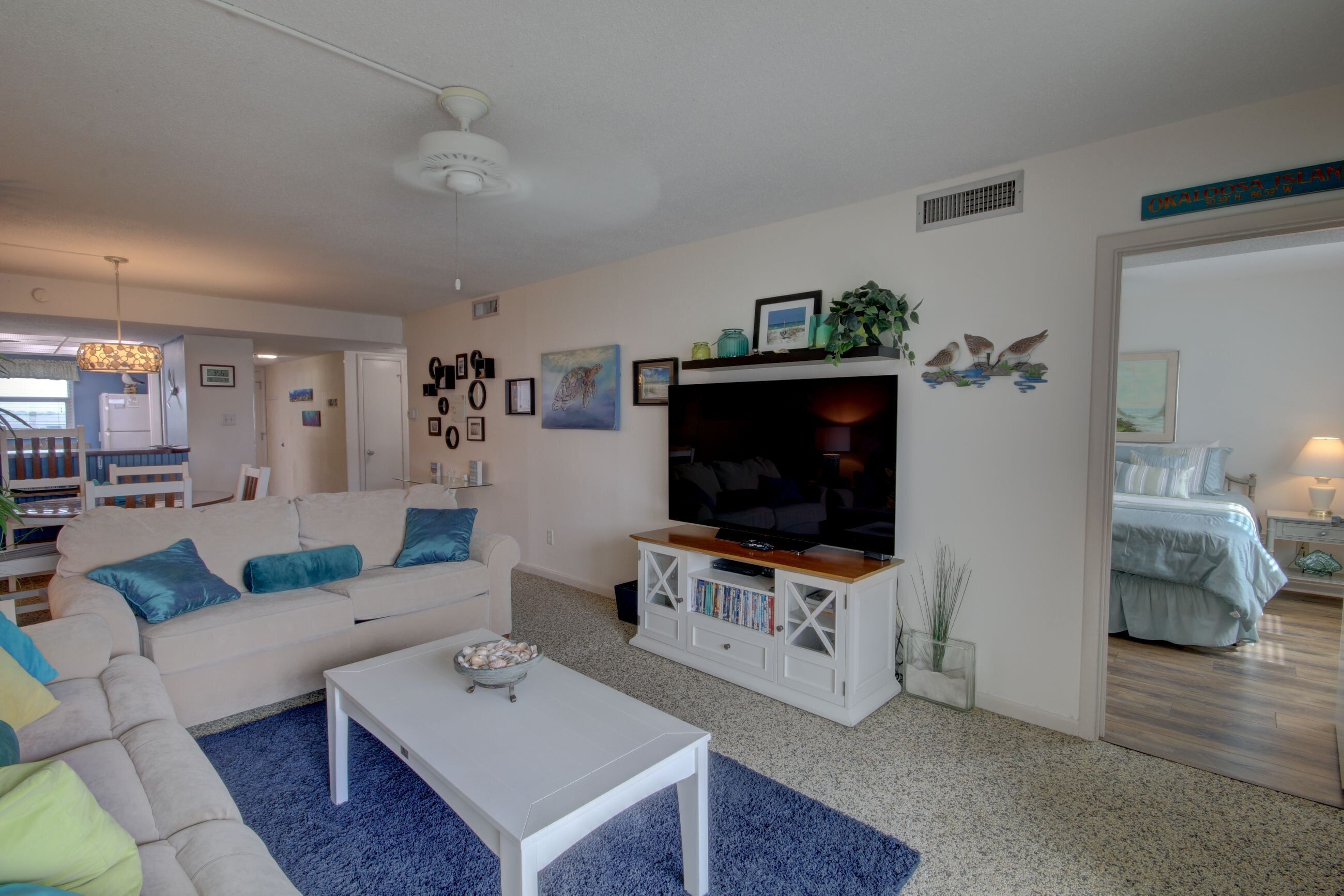 A living room with a white sofa, a coffee table, a TV on a wooden stand, and a bookshelf.