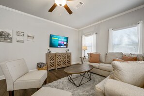 A living room with a sofa, armchairs, a coffee table, a TV mounted on the wall, and a ceiling fan. - 2059 Pinnacle Walk Drive, Norcross (Norcross)