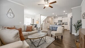 A modern living room with a sofa, coffee table, and chairs, a kitchen in the background, and a ceiling fan. - 2059 Pinnacle Walk Drive, Norcross (Norcross)