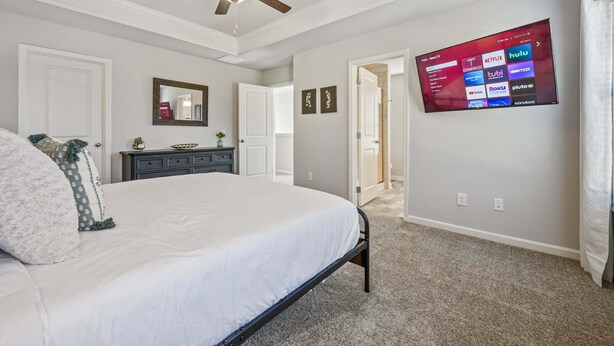 A bedroom with a bed, a dresser, a ceiling fan, a TV mounted on the wall displaying various streaming services, and a door leading to another room. - 2059 Pinnacle Walk Drive, Norcross (Norcross)