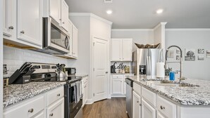 A modern kitchen with white cabinetry, a stainless steel refrigerator, a built-in oven, and a granite countertop. - 2059 Pinnacle Walk Drive, Norcross (Norcross)