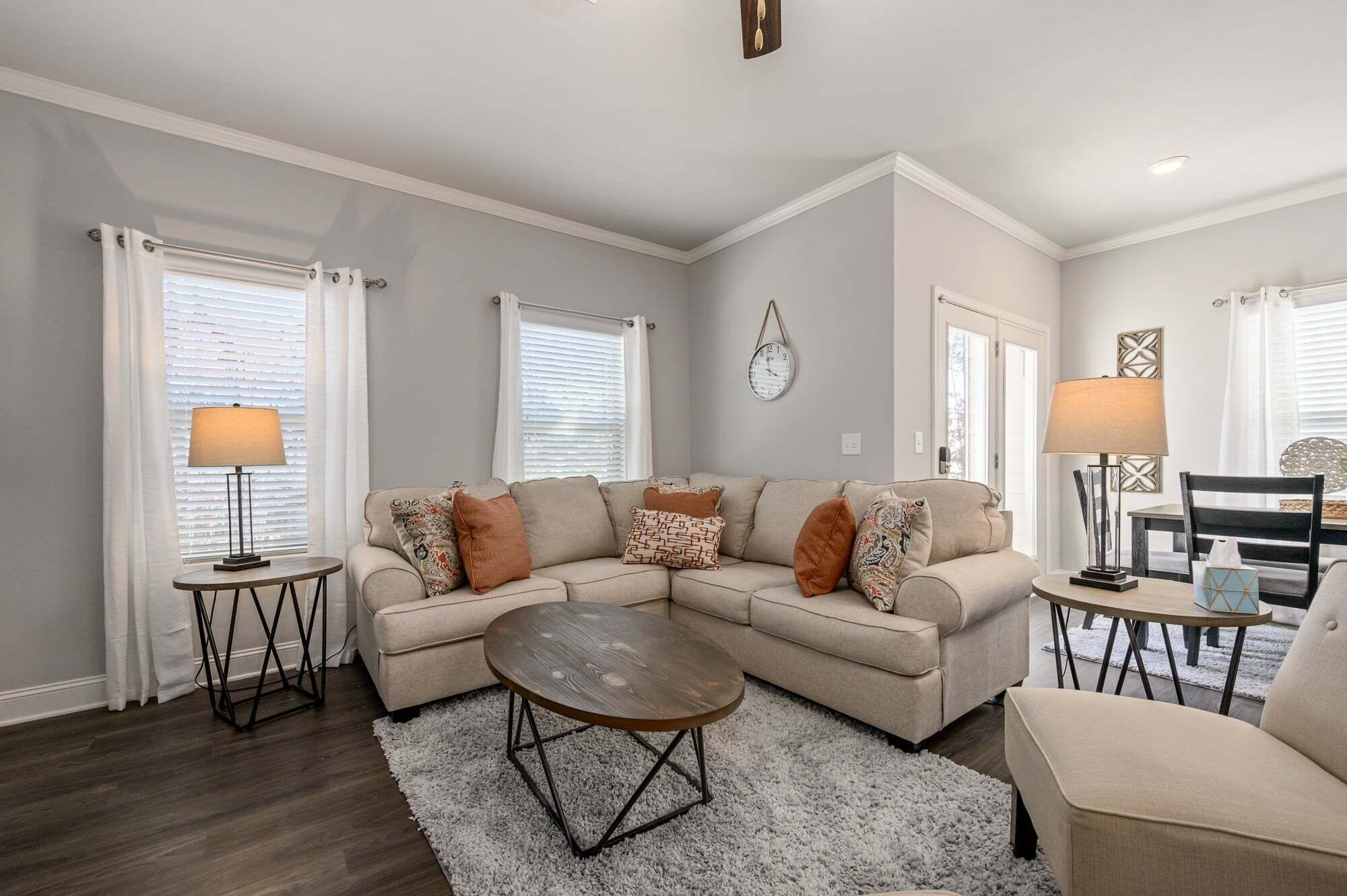 A living room with a sectional sofa, two side tables with lamps, a coffee table, and a clock on the wall.