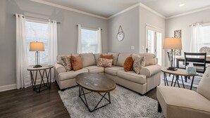 A living room with a beige sectional sofa, two side tables with lamps, a coffee table, and a dining area with a table and chairs. - 2059 Pinnacle Walk Drive, Norcross (Norcross)