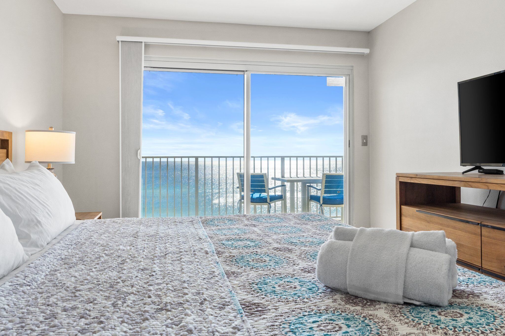 A hotel room with a bed, a TV, a desk, a chair, and a balcony with a view.
